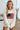 Woman wearing a cream sweatshirt with an American flag design indoors.