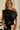 Woman wearing a black off-shoulder top with a gold belt and clutch against a white background
