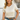 Woman wearing a beige short-sleeve top and blue jeans, standing indoors.