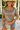 Woman wearing a patterned top and denim shorts against a white wall