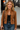 Woman wearing a brown jacket, black top, and blue jeans with a blurred background