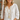 Woman wearing a white embroidered blouse with a necklace, standing indoors.