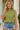 Woman wearing a green sleeveless top and denim shorts, holding a beige clutch.