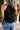 Person wearing a black tank top and blue jeans against a gray textured wall